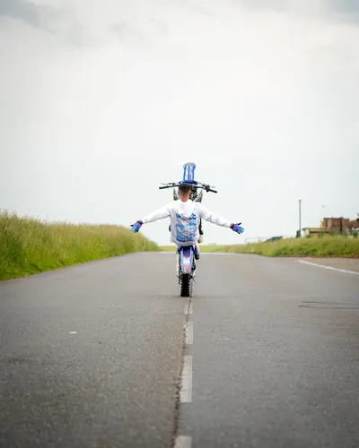Arms outstretched in total control, the rider balances a wheelie along the centre line of an empty road.