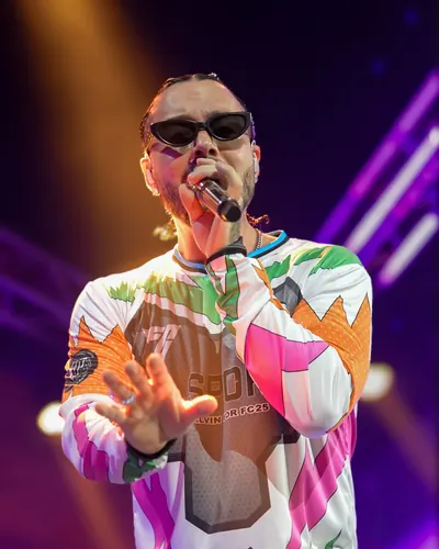 Low-angle portrait of J Balvin reaching toward the lens, his vivid EA Sports FC jersey glowing against purple beams.